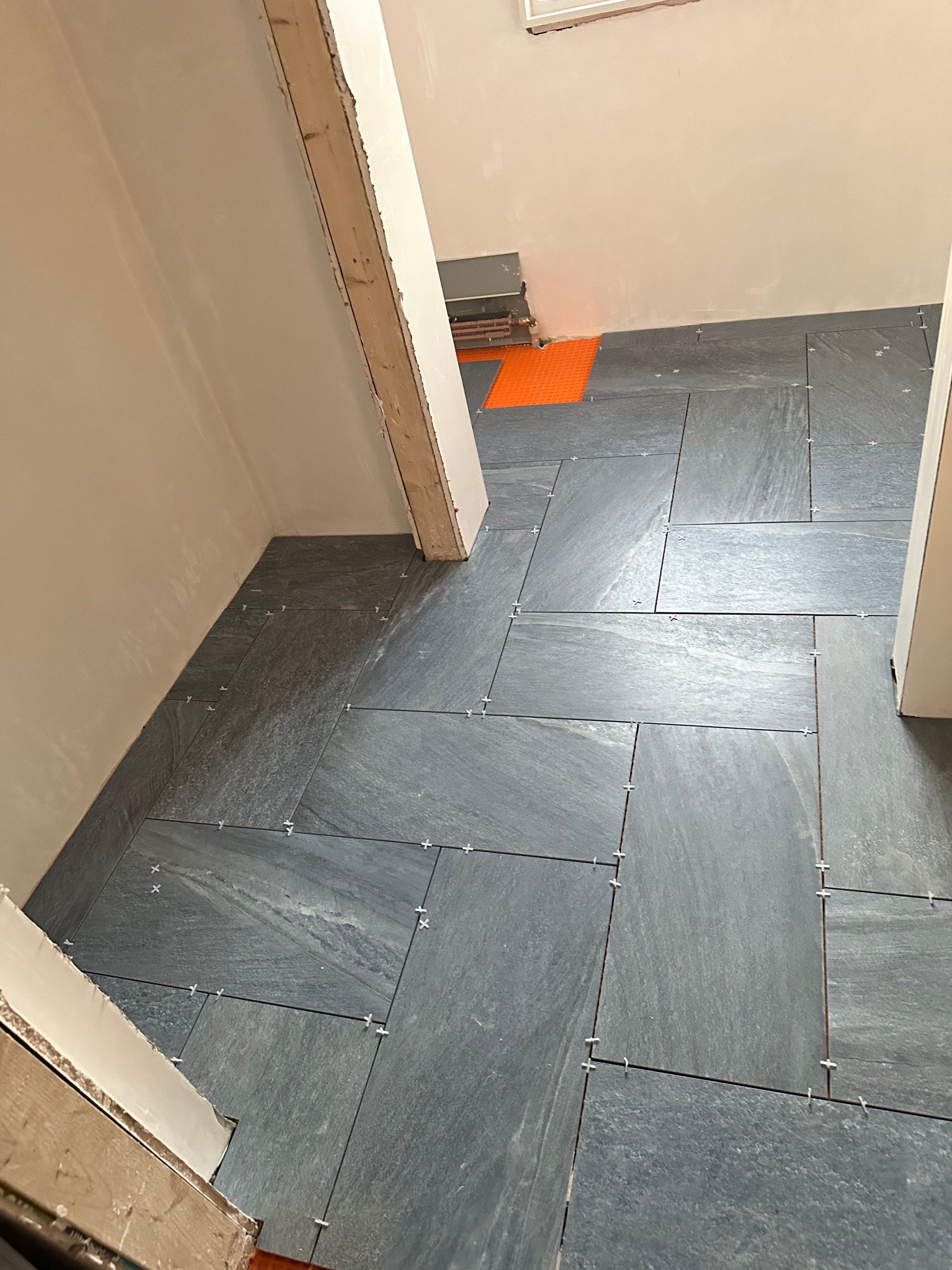Floor with interconnected gray tiles being installed in a doorway. Orange marking visible.