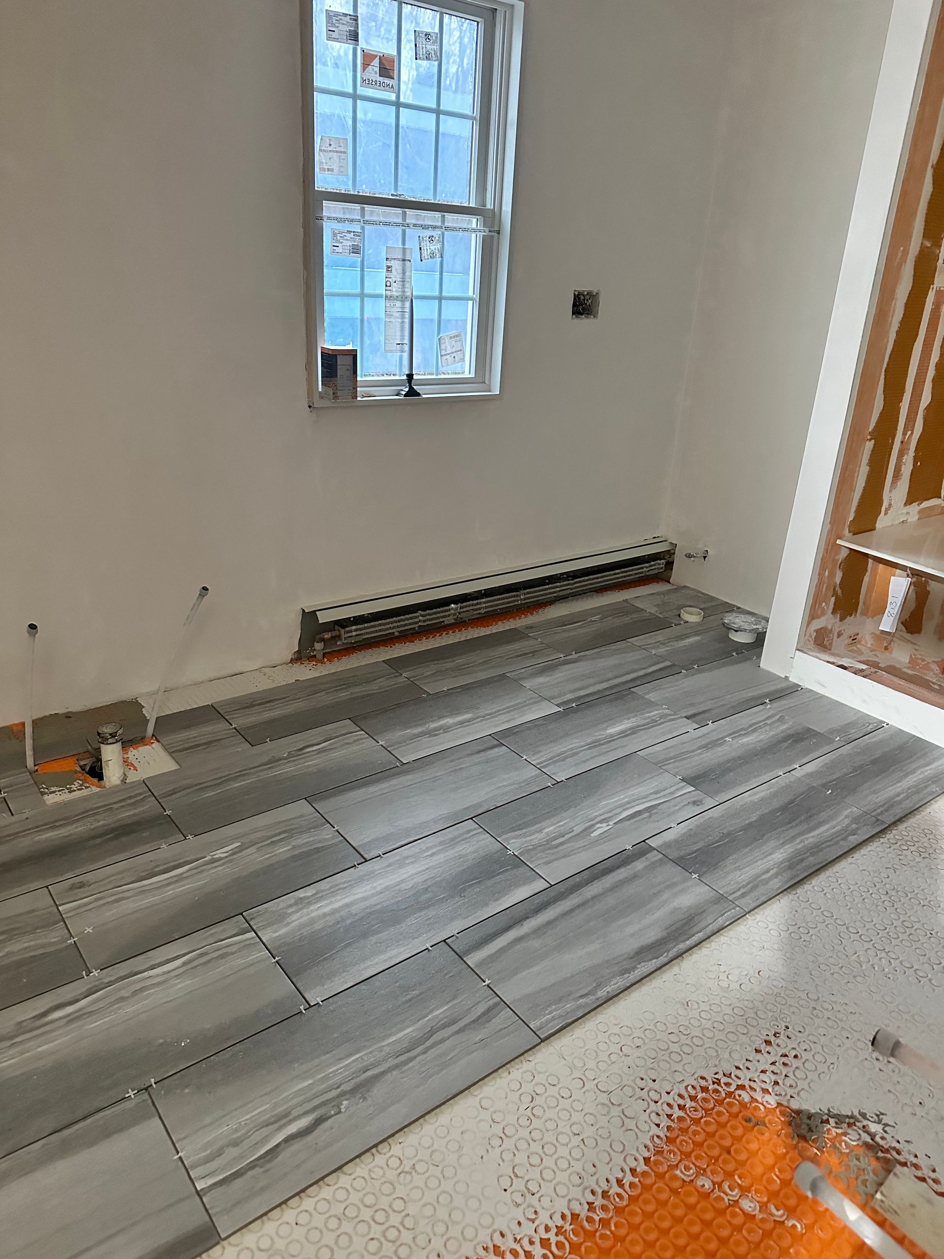 Room with floor tile installation in progress; gray tiles laid on white mortar, near a window.