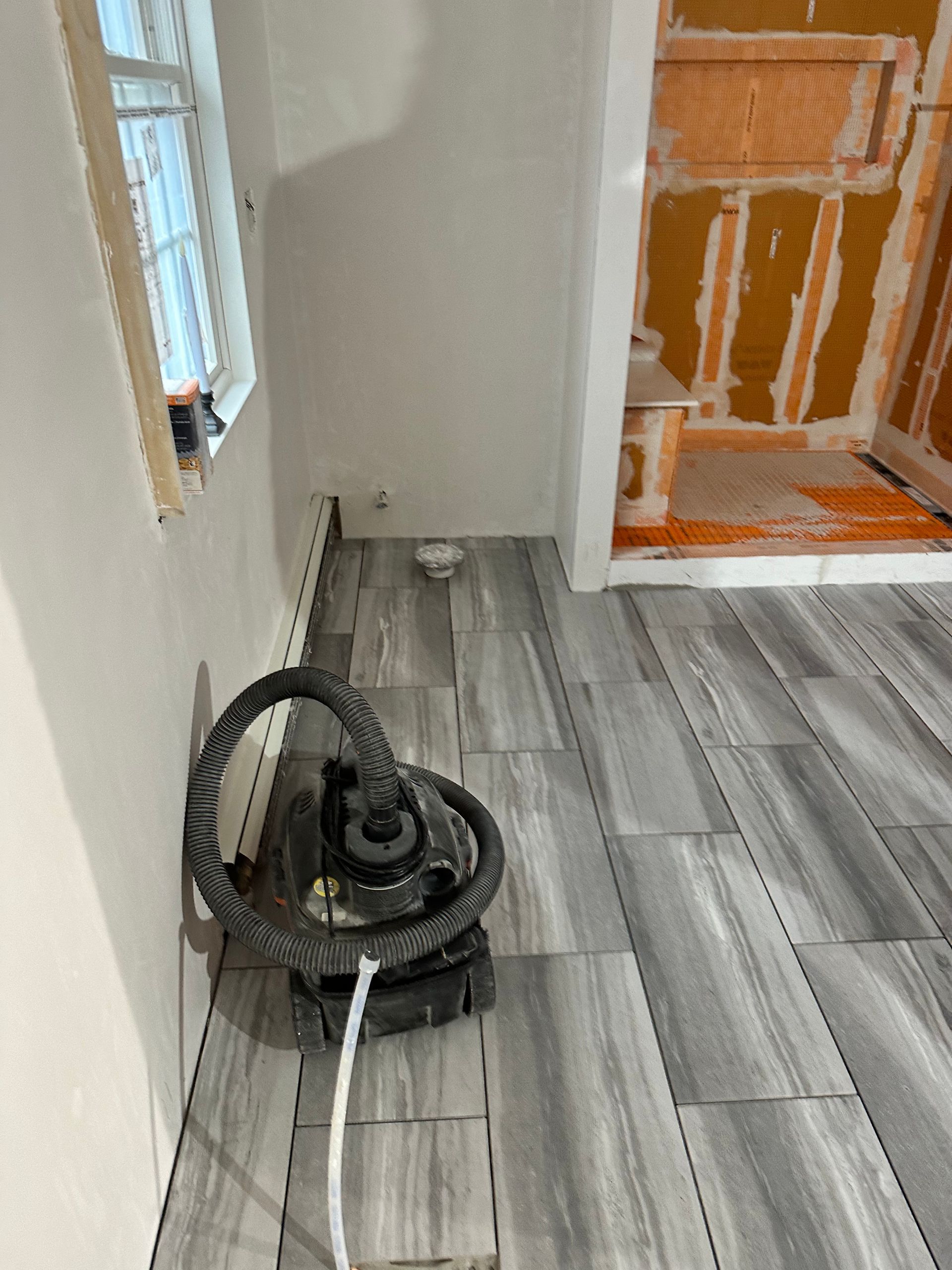 Newly tiled floor in a room with a window, doorway, and a vacuum cleaner on the tiles.
