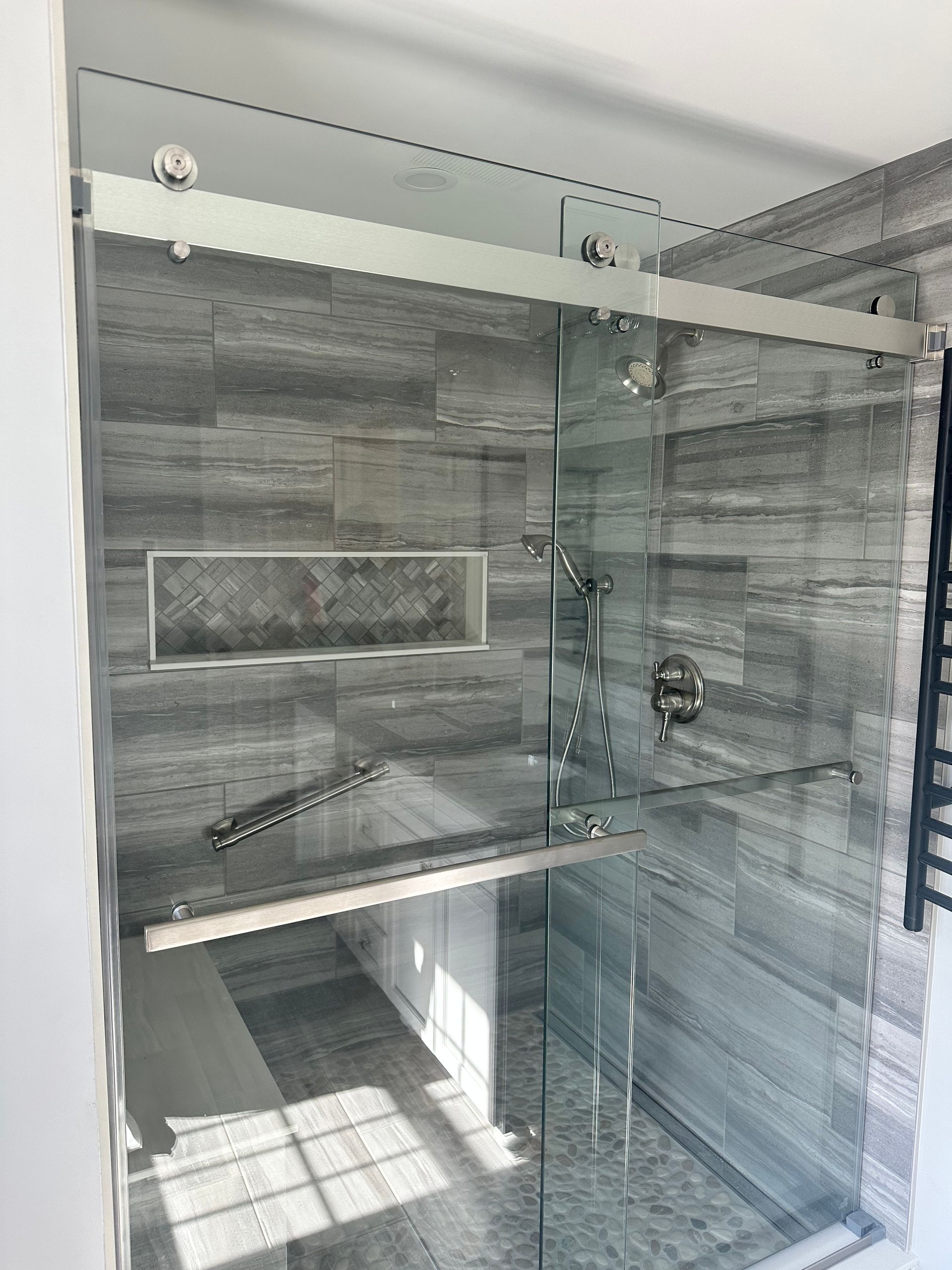 Glass shower with sliding door, gray tile walls, and a recessed shelf.