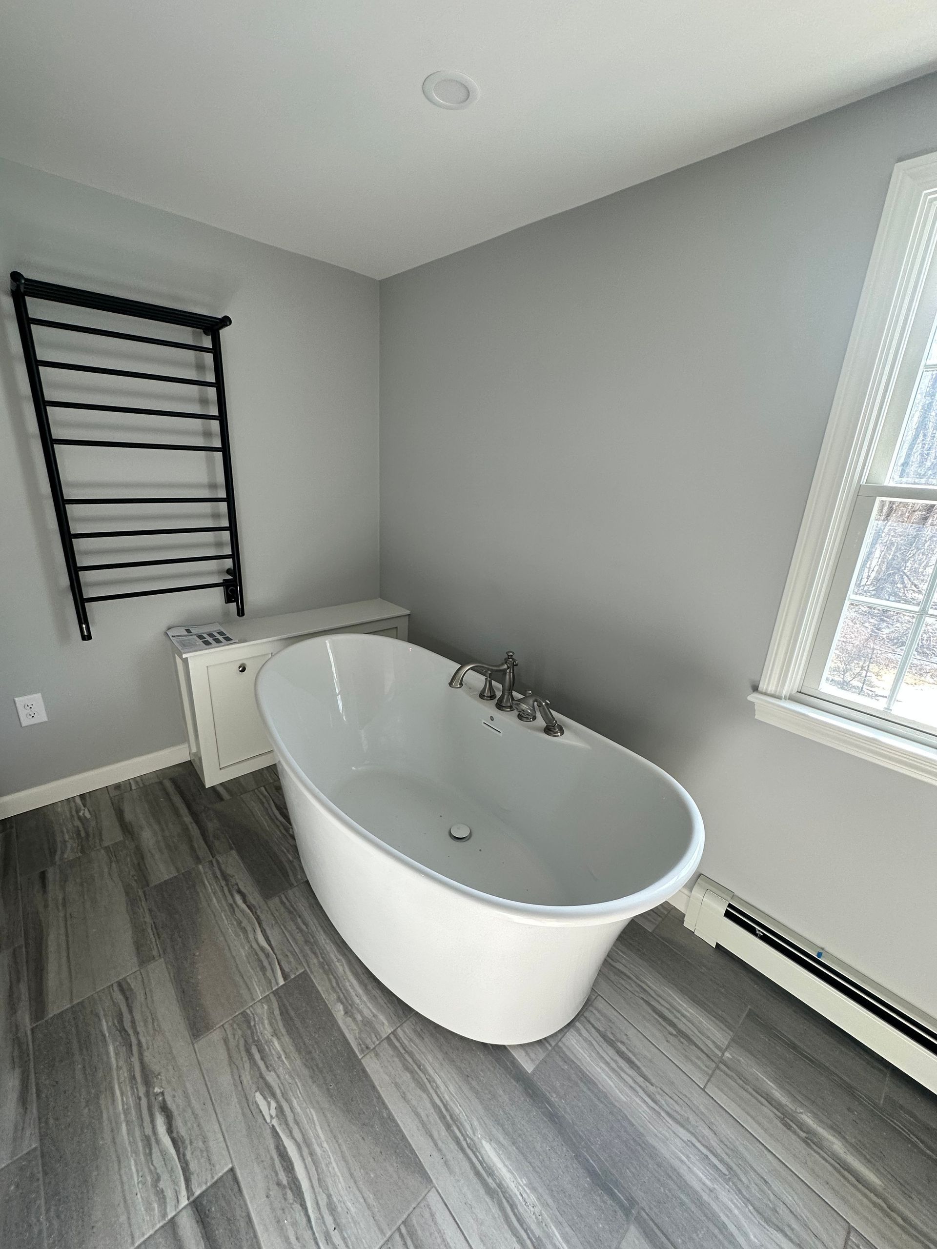 Bathroom with freestanding white tub, heated towel rack, gray walls, and wood-look flooring.