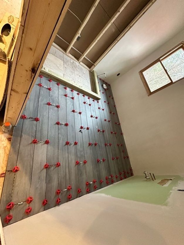 Tiled wall under construction, with leveling clips in place. Room shows unfinished ceiling, floor, and a small window.