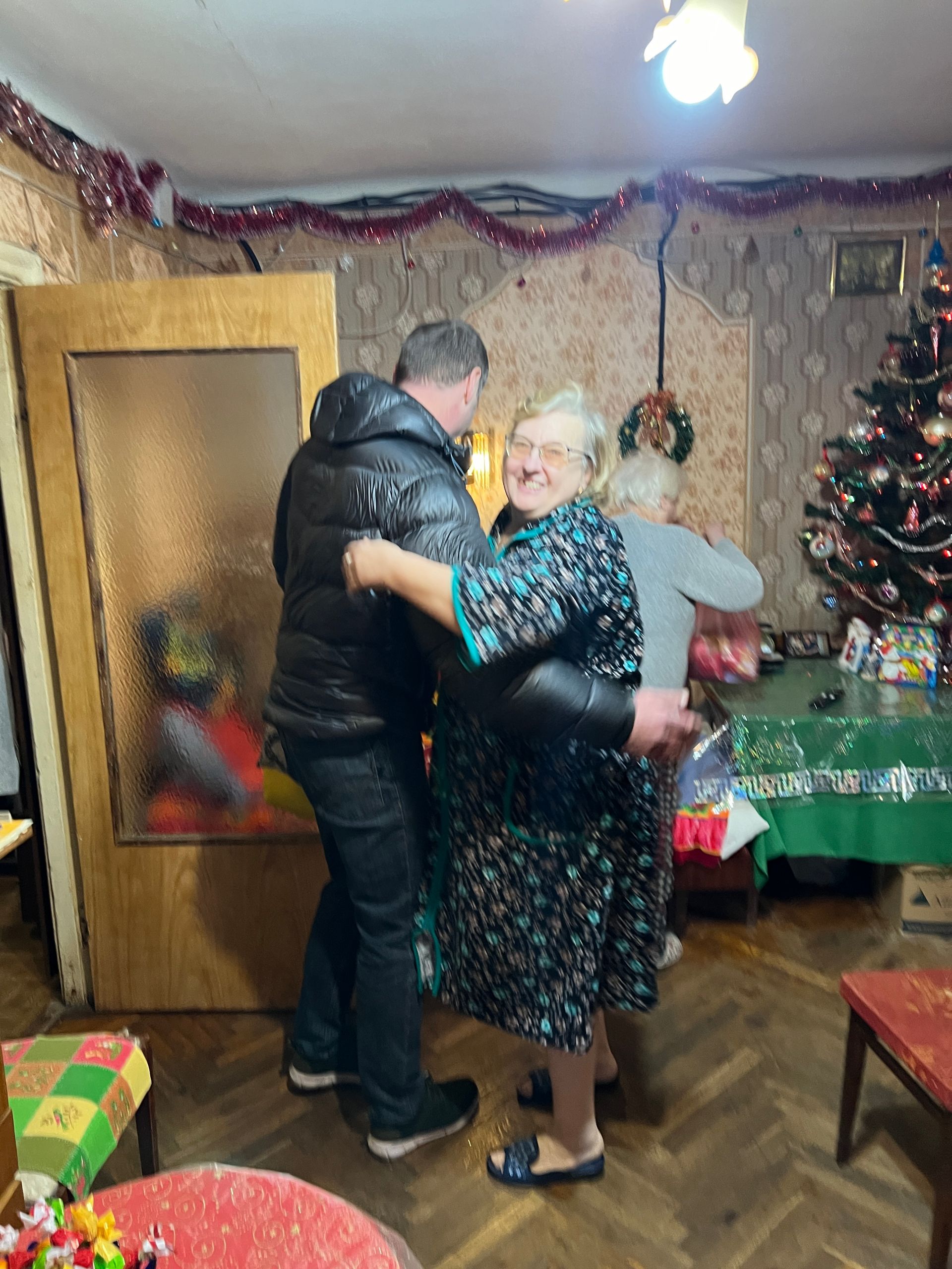 Mann danser med to kvinner i et rom pyntet til jul.