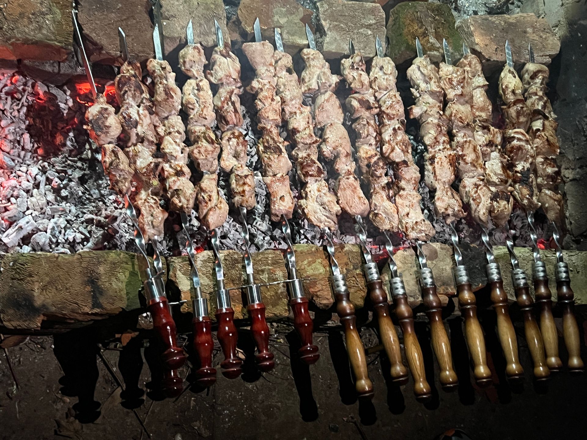 Kjøttspyd grillet over glødende kull i en grillgryte av murstein.