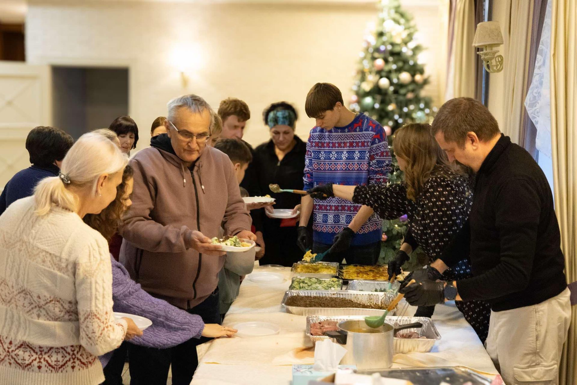 Folk ved et buffetbord som velger mat. Juletre i bakgrunnen.