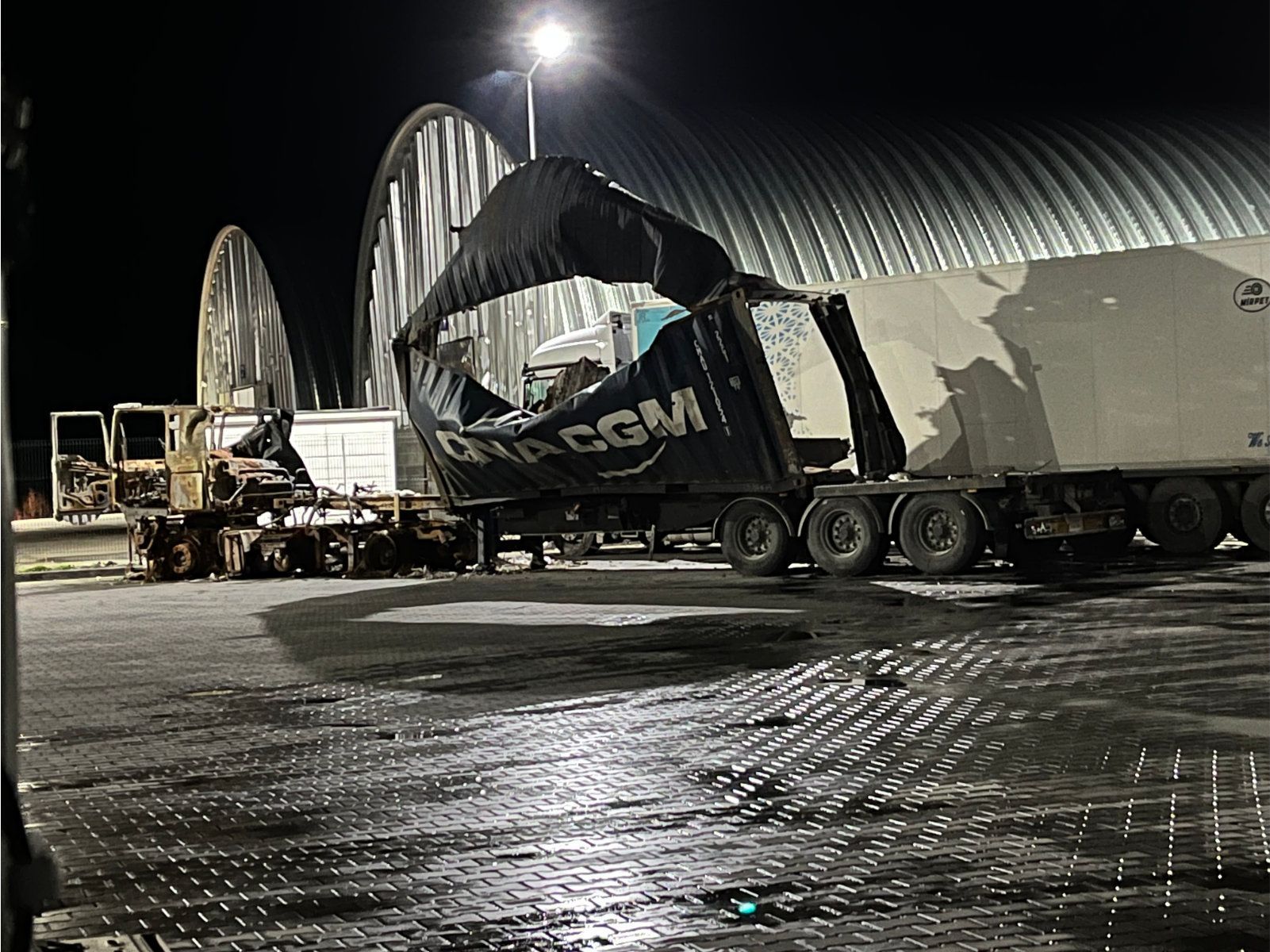Semitrailer med revet deksel, parkert om natten i nærheten av en stor bygning.