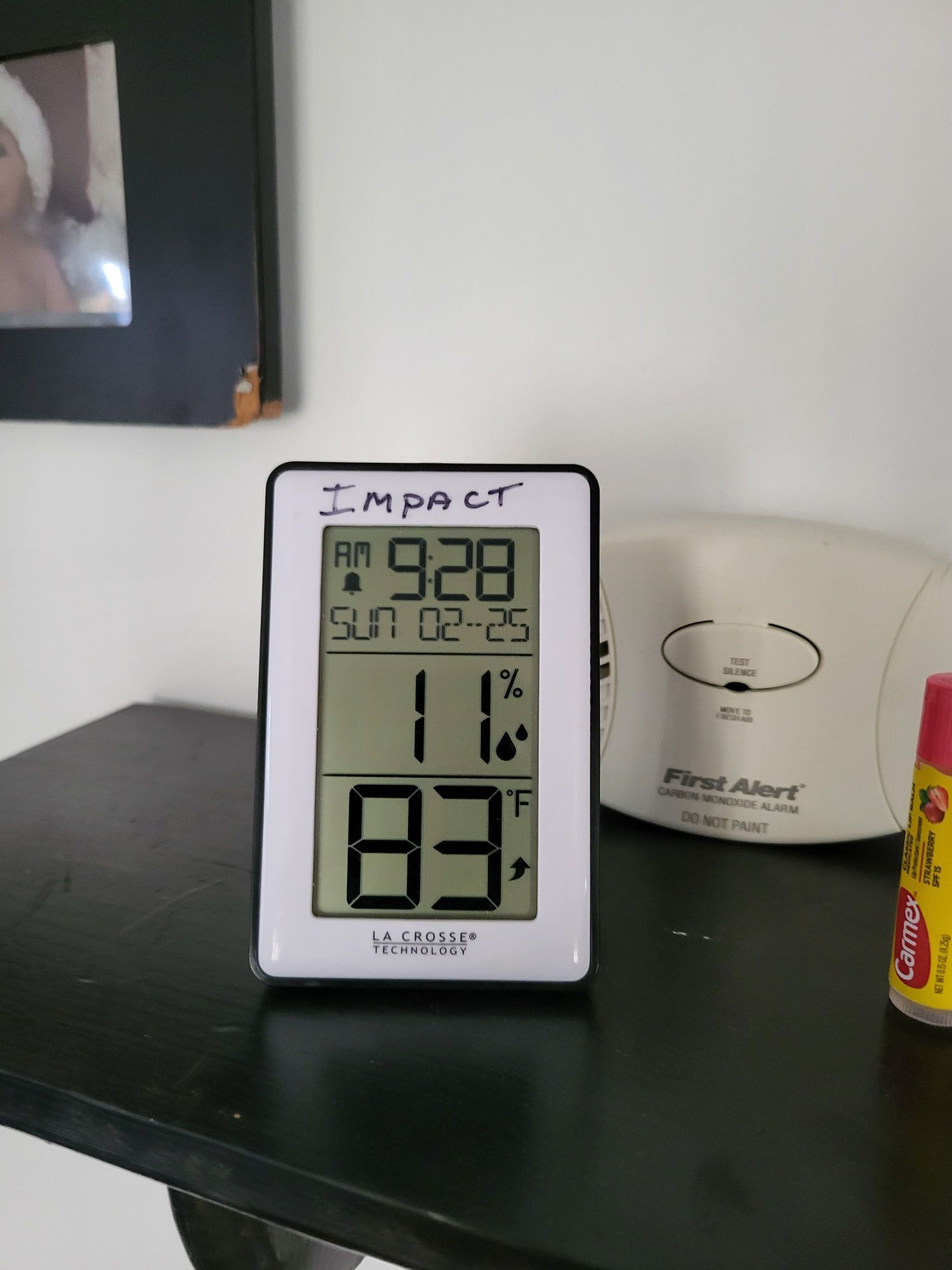 Digital thermometer-hygrometer on a dark shelf beside a white appliance and yellow canister
