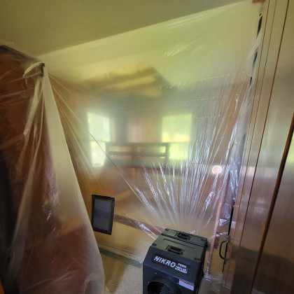 Room under renovation, covered in clear plastic sheeting with a black air purifier in the foreground.