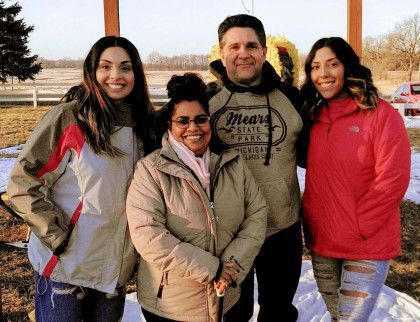 Four people smiling outdoors in winter jackets, standing together in a park at sunset.