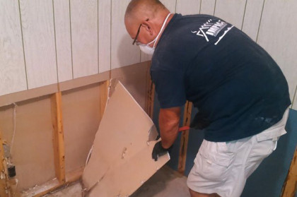 Man in a dark shirt and white shorts installing drywall in a partially finished room