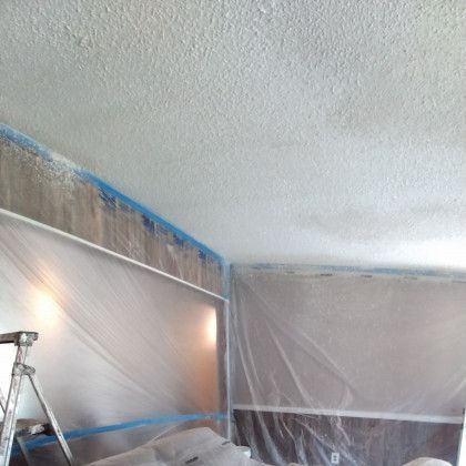Living room under renovation with plastic sheeting, blue painter’s tape, and a step ladder