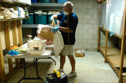 Man in a basement workshop pours materials into a clear bag beside a table and tools.
