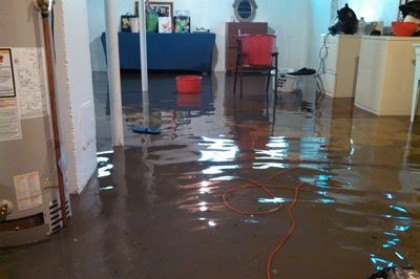 Flooded room with water covering the floor, reflecting furniture and a dangling orange cord.