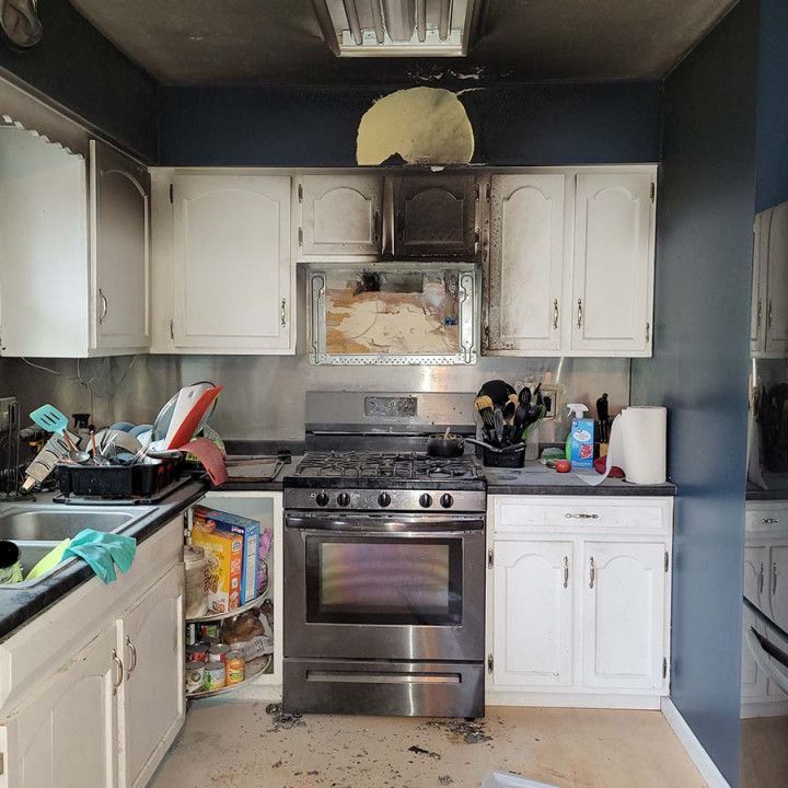 Cluttered kitchen with white cabinets, stainless steel stove, and dishes piled on counters