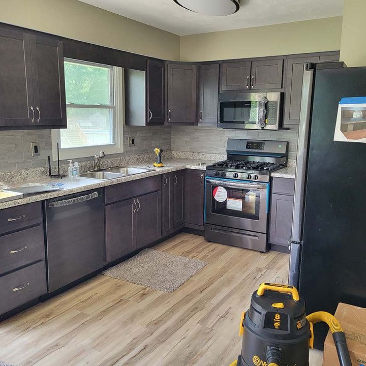 Modern kitchen with dark cabinets, stainless appliances, light wood floor, and a vacuum in the foreground