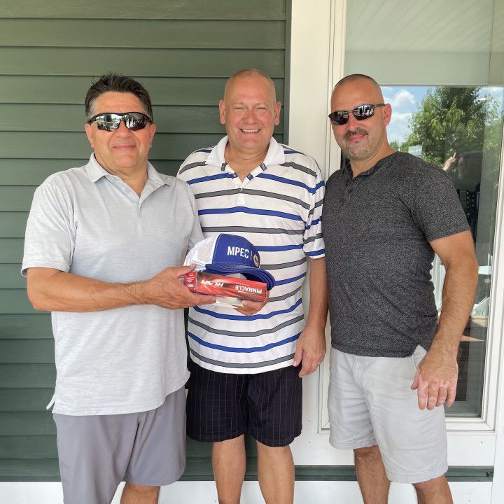 Three men standing on a porch, smiling and holding a Miller hat