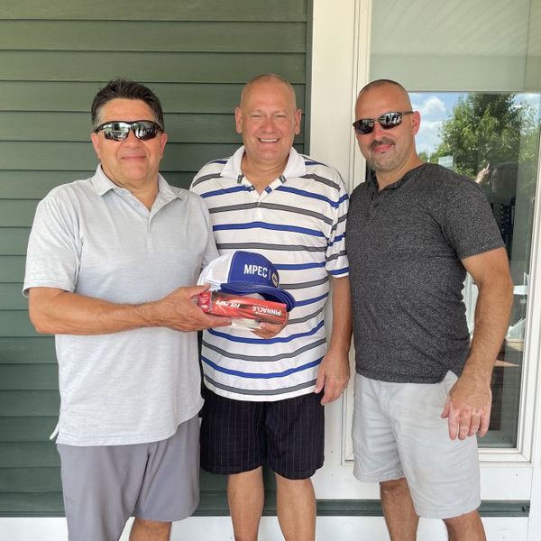 Three men standing on a porch holding a Miller beer pack