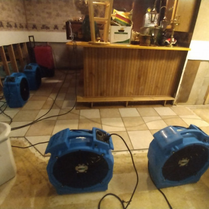 Two blue floor fans on a tiled floor in a room with a wooden bar counter and cables on the ground