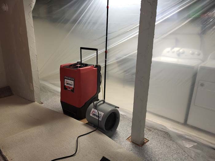 Dehumidifier and box fan in a plastic-covered room, with a cord on the carpet.