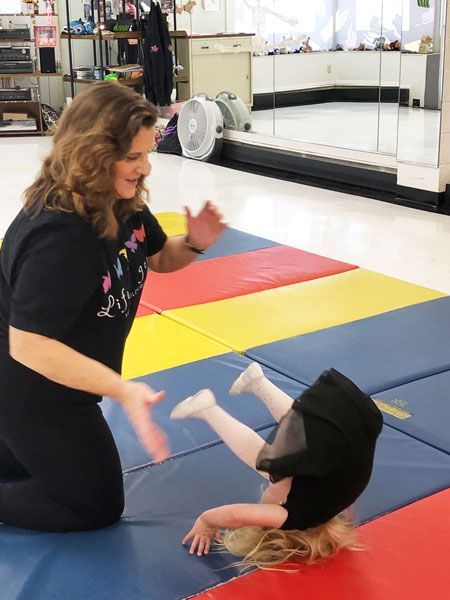 Instructor guiding a child on colorful mats in a dance studio
