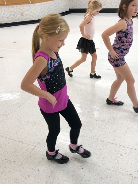 Children practicing dance moves in a studio, wearing leotards and tap shoes.