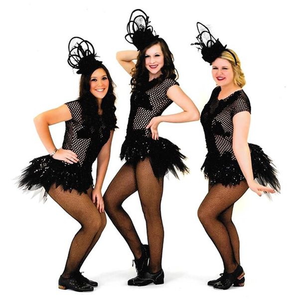 Three performers in black sequined outfits and feathered skirts pose against a white background.
