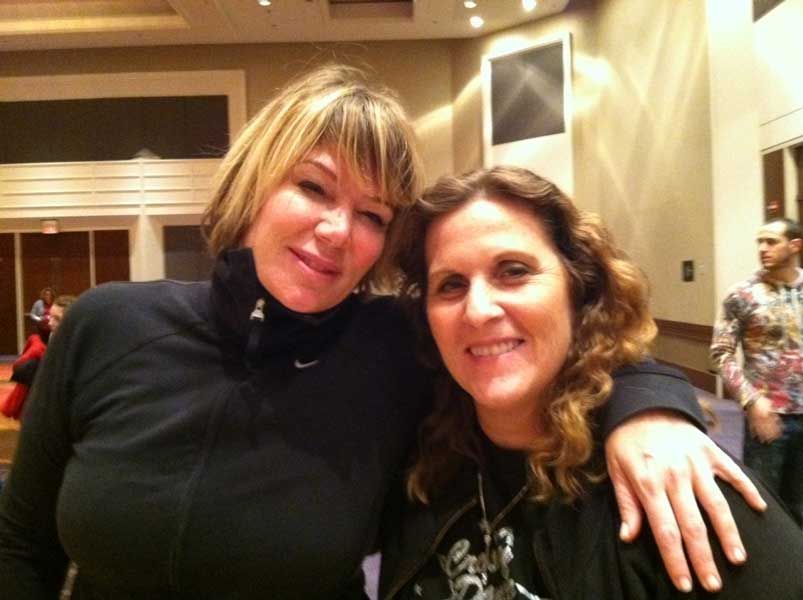 Two women smiling and posing together indoors at a warmly lit event
