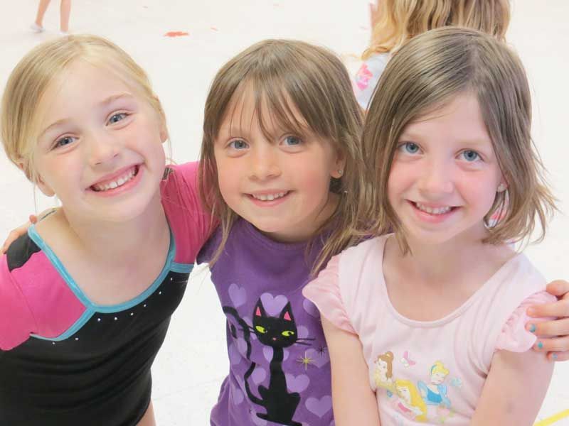 Three smiling children posing together in colorful shirts