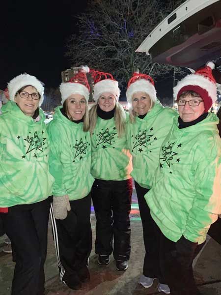 Five people in green hoodies and Santa hats posing together outdoors at night.