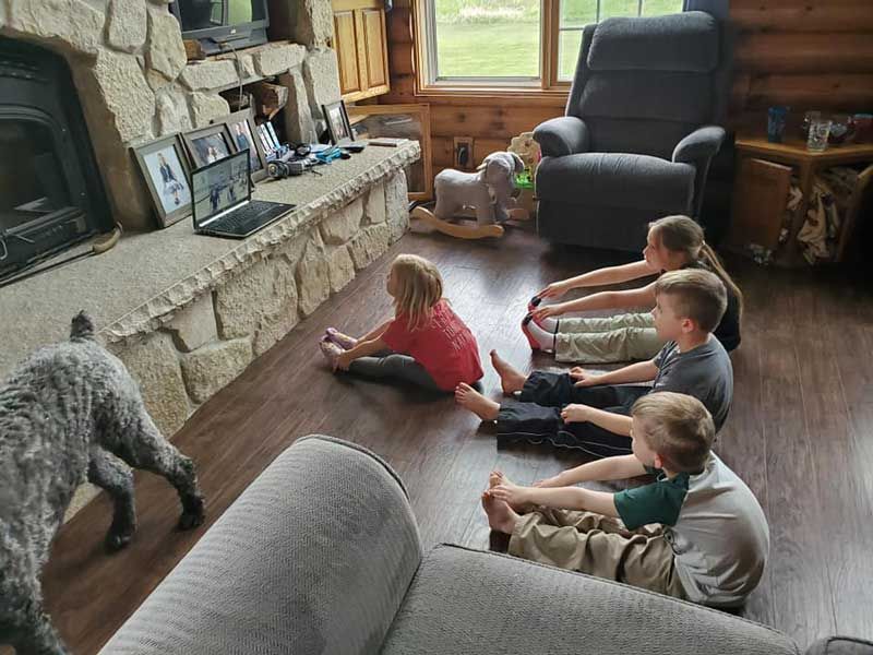 Children stretching on a wooden floor near a stone fireplace