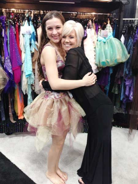 Two women hugging in a dress shop, surrounded by colorful dresses and formal gowns