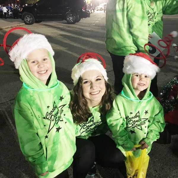 Three people in green hoodies and Santa hats posing together at a nighttime holiday event.