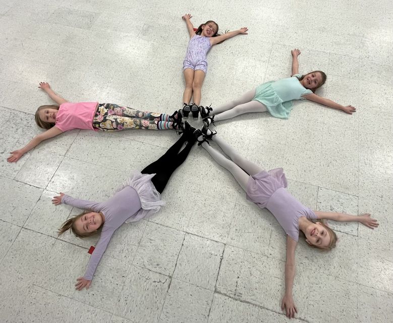 Five children lie in a circle on the floor, arms outstretched
