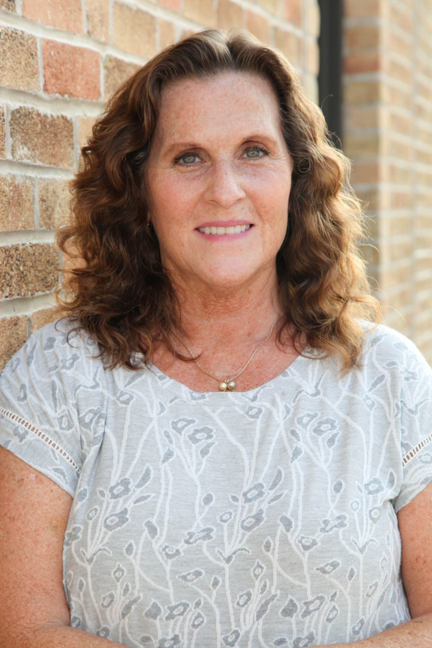 Portrait of a smiling person in a white lace top standing against a brick wall