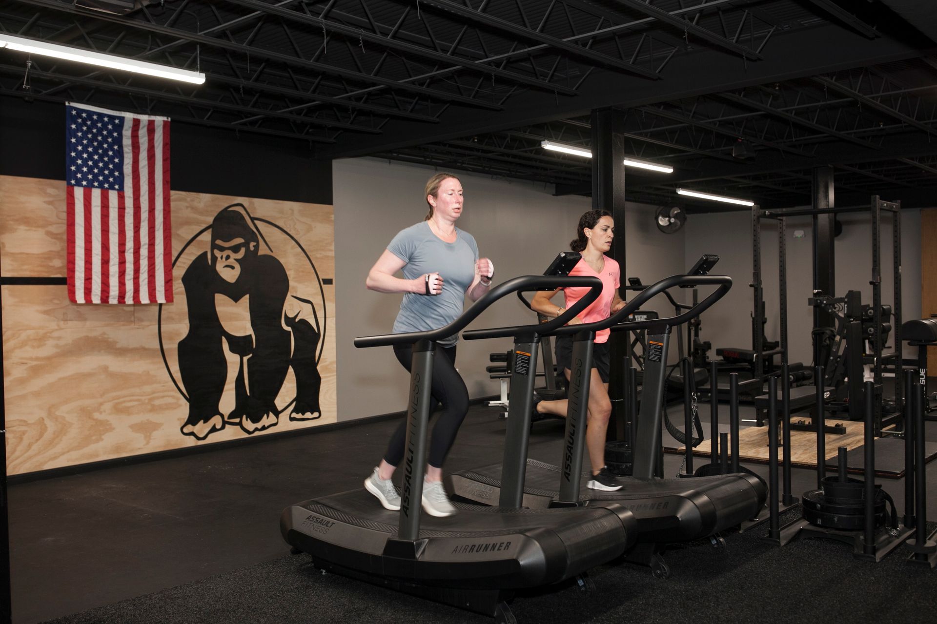 Two people running on curved treadmills in Vitality Athletics in Ephrata, PA with an American flag and gorilla logo.