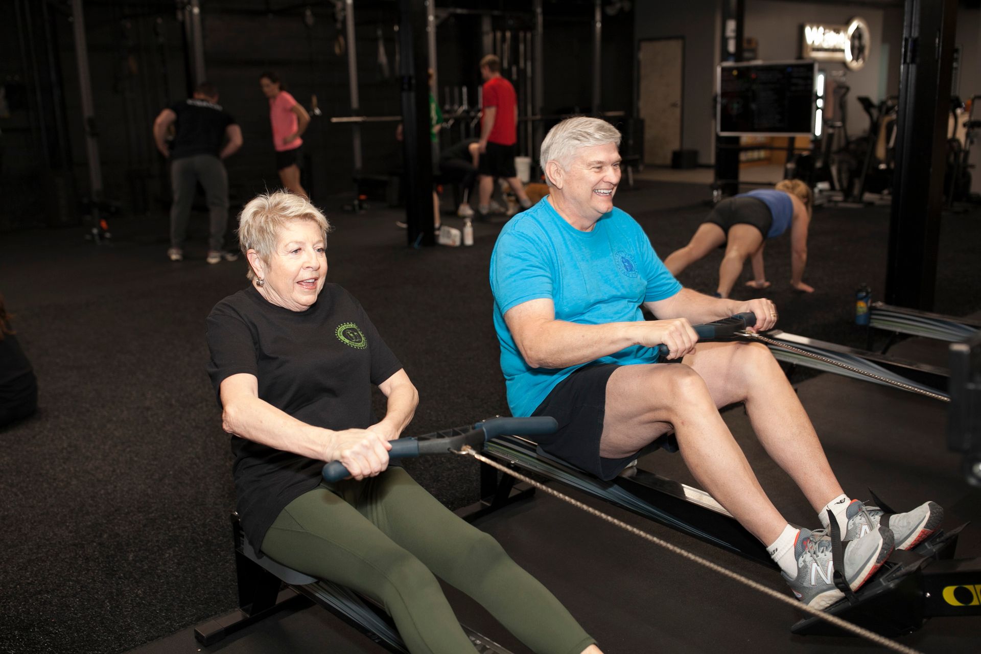 Two people rowing on machines at Vitality Athletics in Ephrata, PA. Others are exercising in the background.