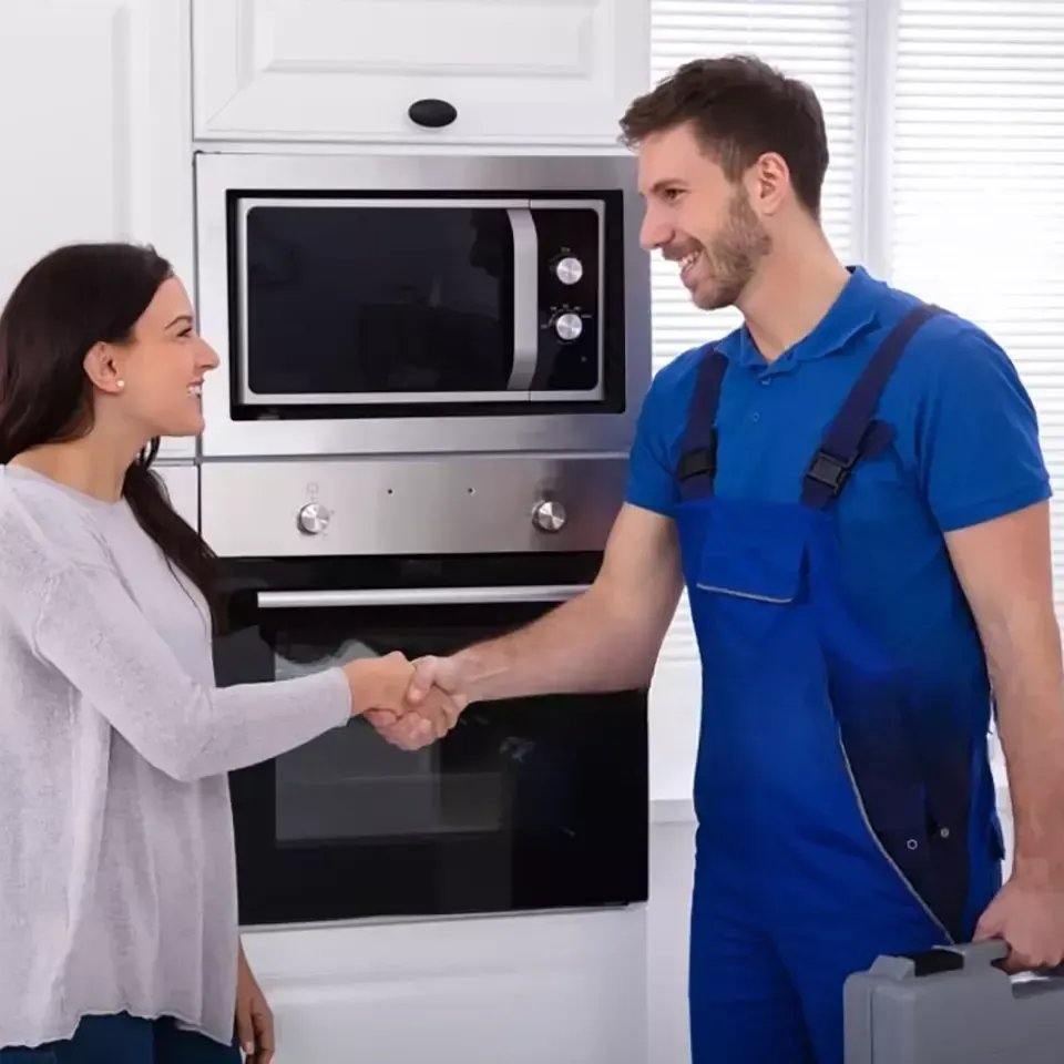 Woman shakes hands with a repairman in front of a microwave and oven. Both smile.