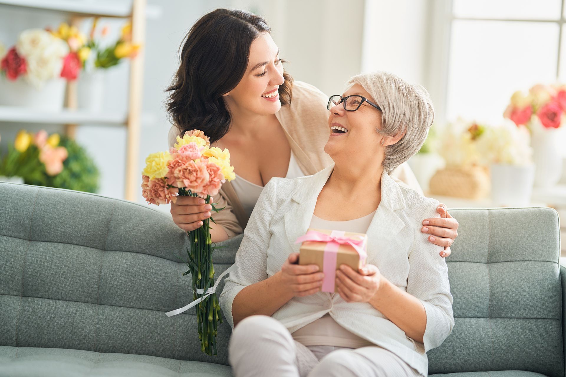 A woman is giving a gift to an older woman who is sitting on a sofa.