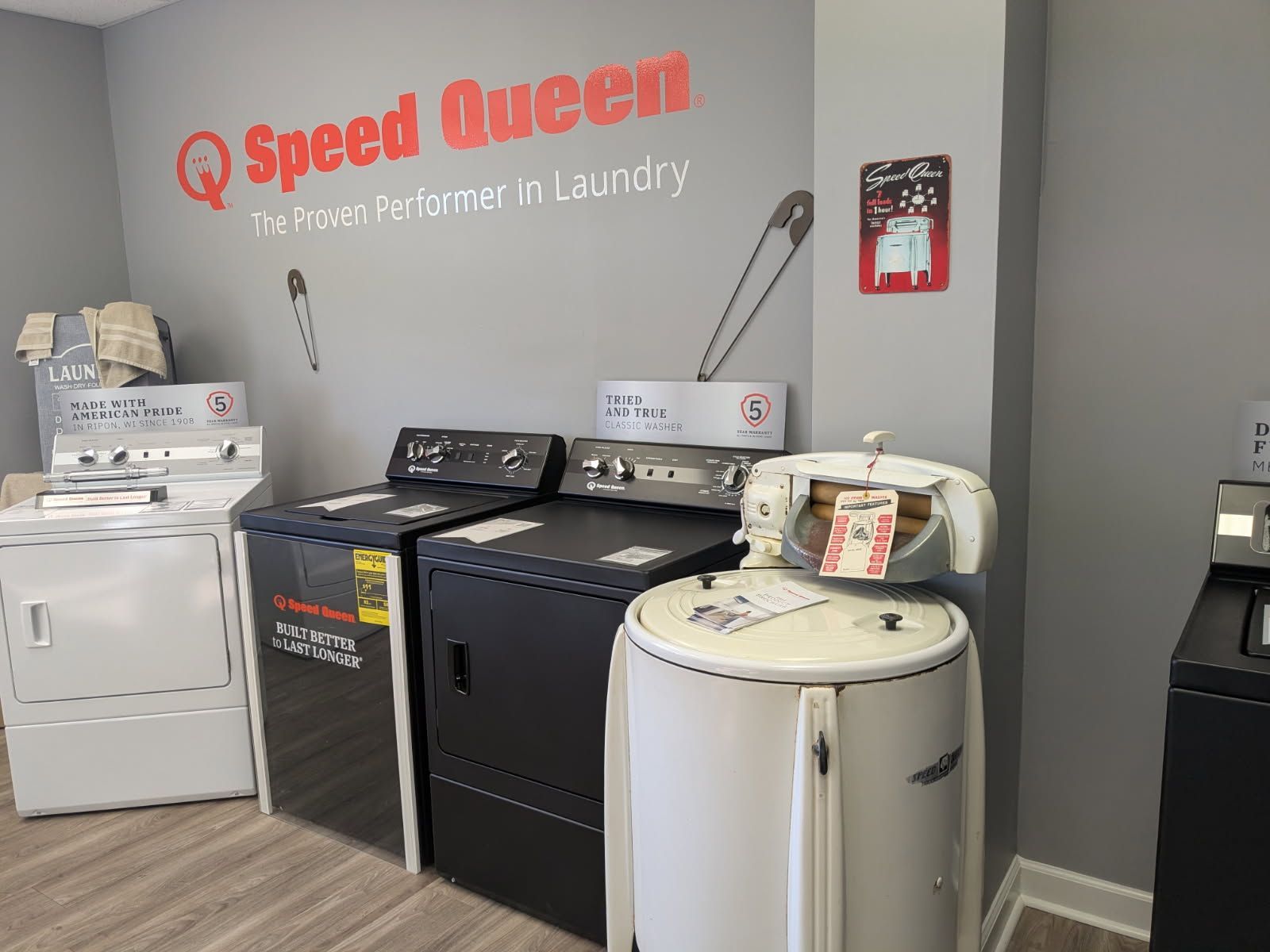 Laundry room with several washers and dryers under a “Speed Queen” sign on a gray wall.