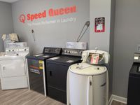 Laundry room with several washers and dryers under a “Speed Queen” sign on a gray wall.