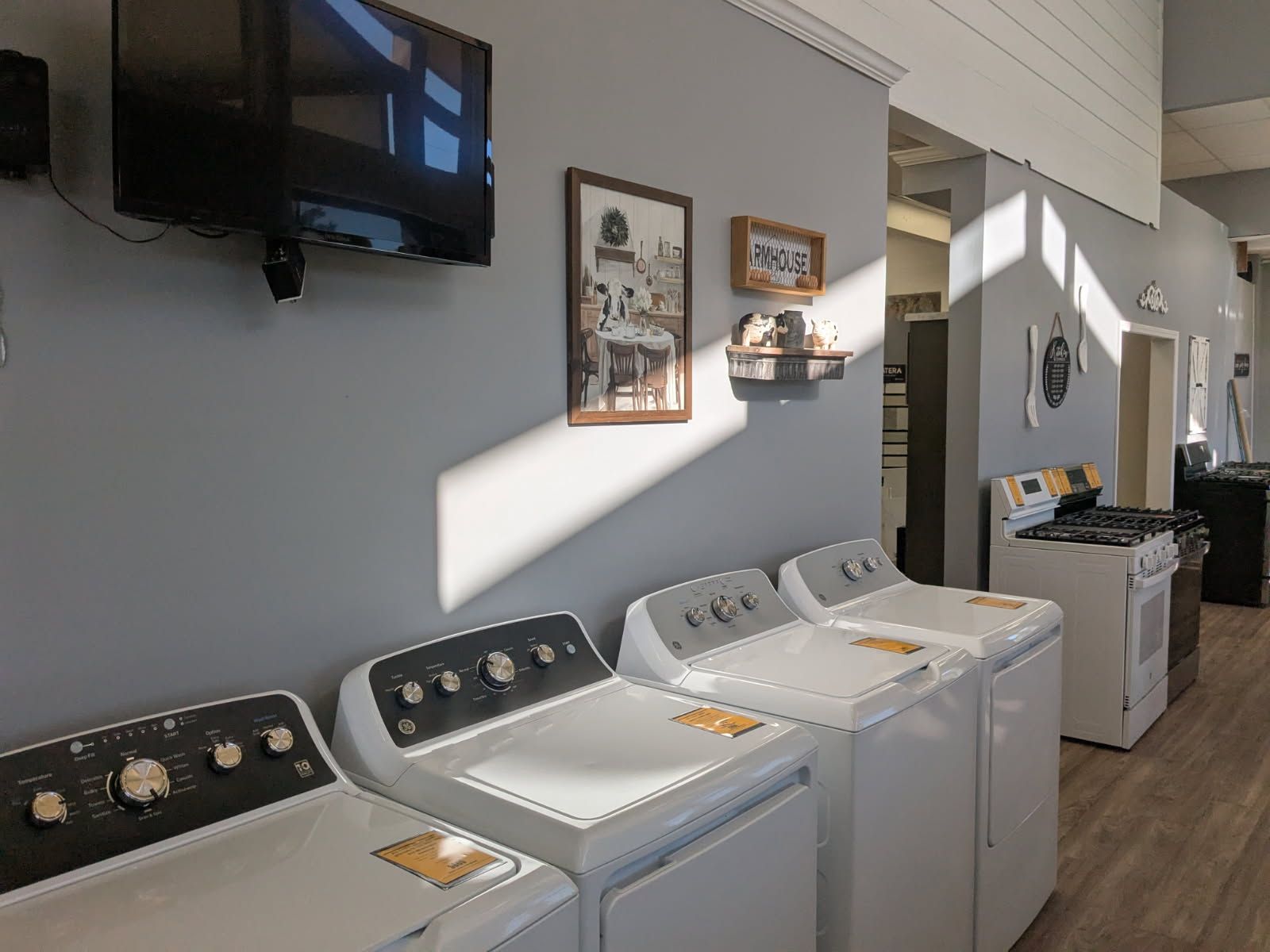 Laundry room with white washers and dryers, gray walls, wall-mounted TV, and framed wall decor.