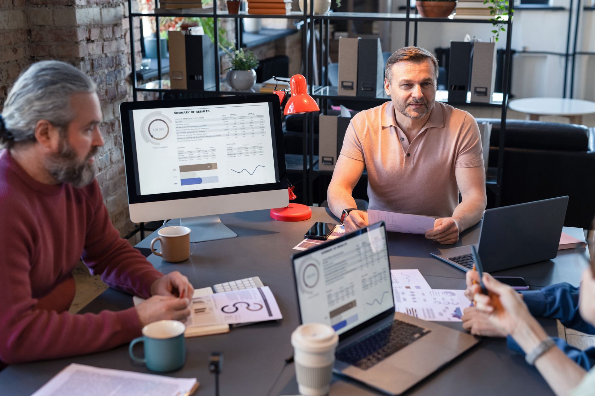 Team meeting around a conference table with laptops, mugs, and a presentation screen in a modern office
