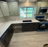 Modern kitchen with gray cabinets, white countertops, black appliances, and a window over the sink.
