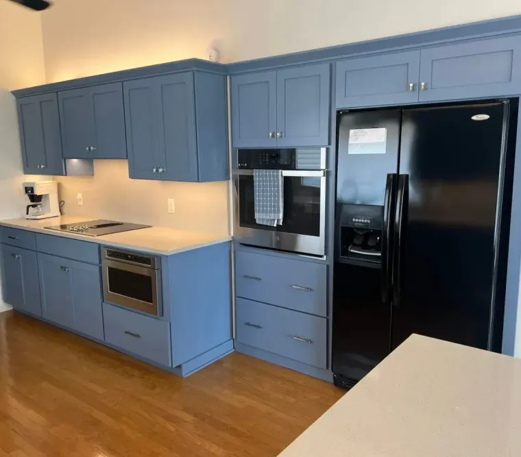Blue kitchen with black appliances, wood floors, and a white countertop