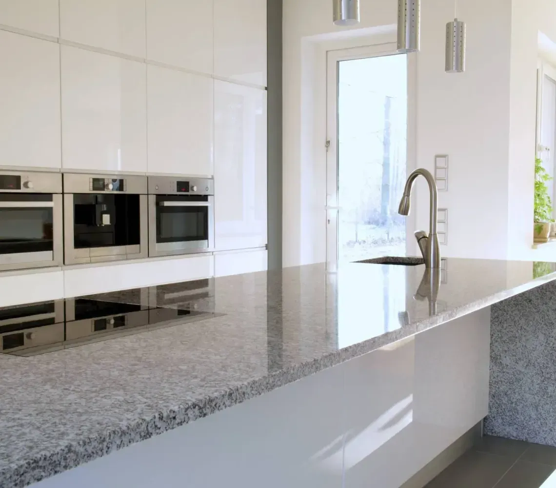 Modern white kitchen with a speckled granite island and built-in ovens