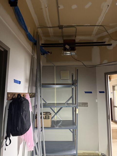 Indoor utility room with metal shelving, hanging coats, exposed ceiling pipes, and a doorway.