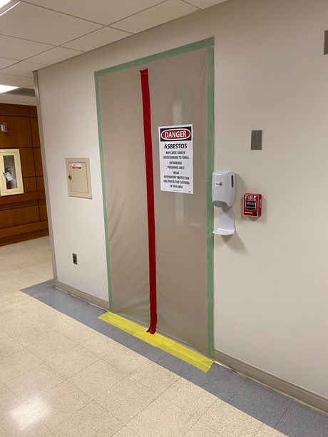 Hospital doorway covered with clear plastic, marked by red and green tape, next to a wall sanitizer dispenser.