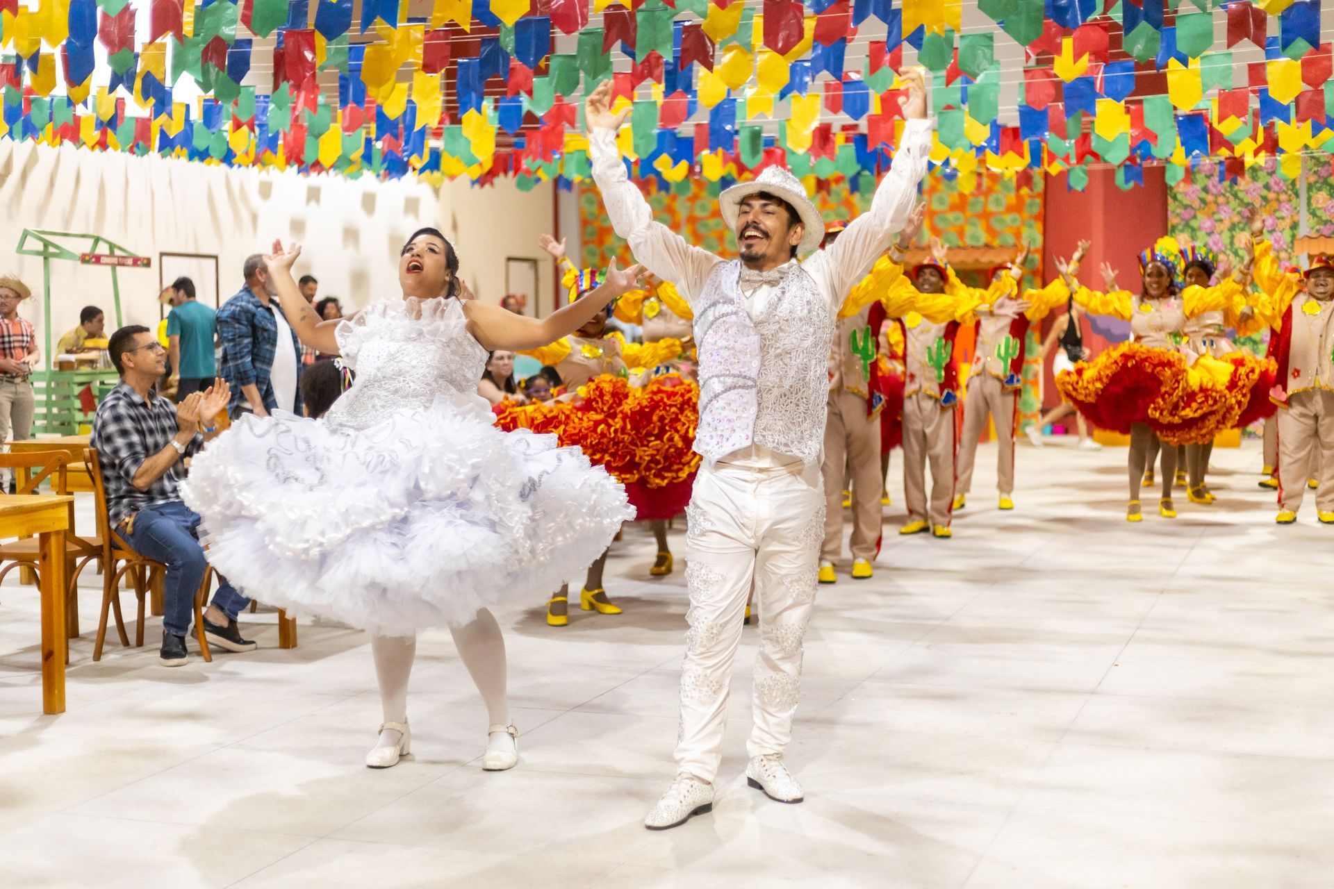 Casal vestido de noivos dançando quadrilha em festa junina decorada no hotel.
