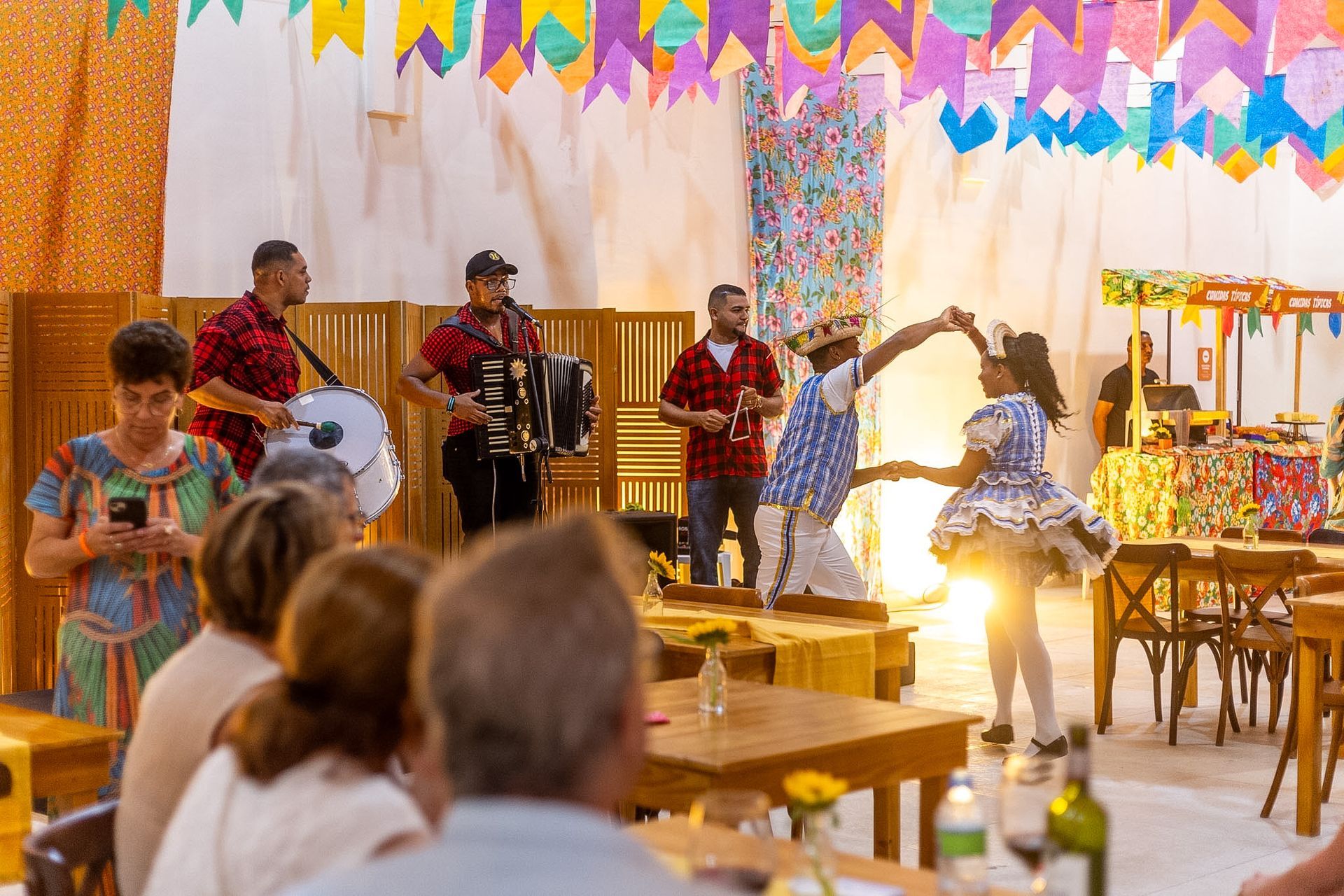 Trio de forró e casal dançando em festa junina do hotel decorada com bandeirinhas.