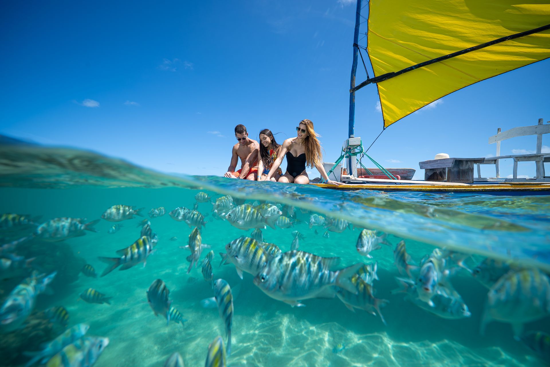 Família em jangada nas piscinas naturais olhando cardume de peixes coloridos.